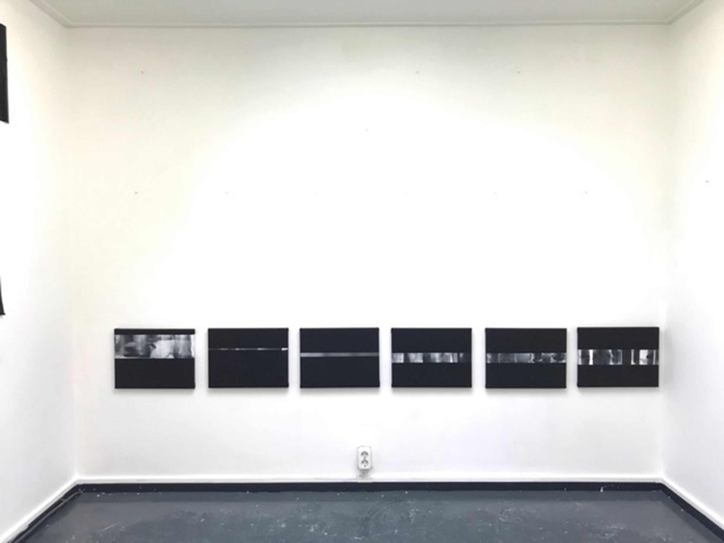zes schilderijen met gradaties van zwart, wit en grijs aan de muur in het atelier